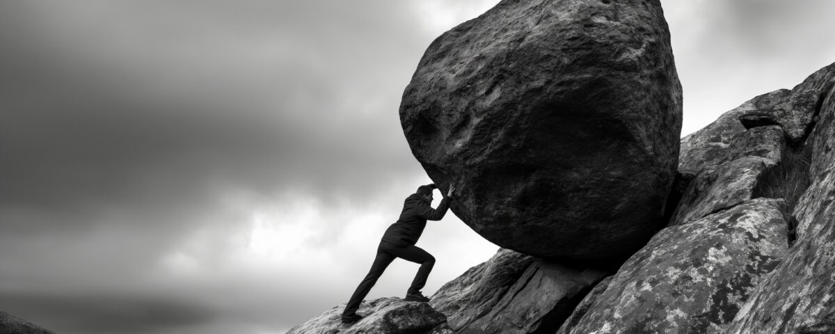 Silhouette man struggles to push massive boulder uphill on rocky terrain image. Overcast sky, rugged landscape photography scene wallpaper. Sisyphean task resilience concept photo